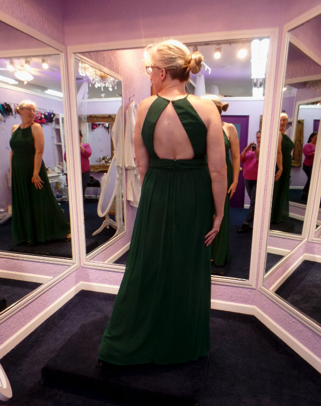 Holly in a full-length halter-top dress, from the back and seen in a 3-way mirror in a fitting room