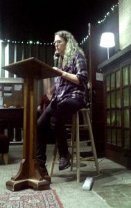 author A.S. King in flannel and jeans, reading at a lectern