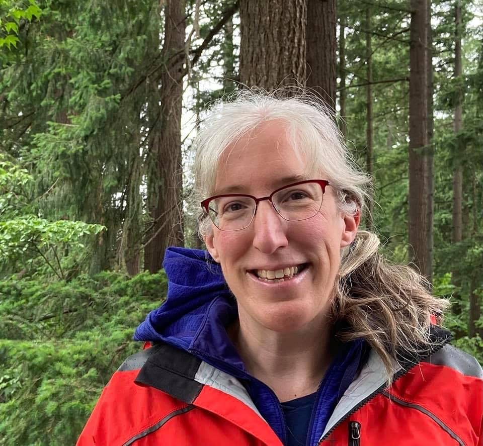 Holly wearing a rain jacket and smiling in a forest