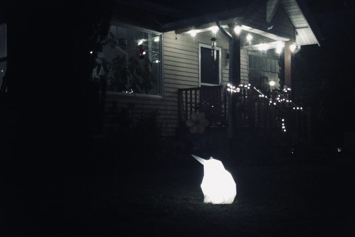Glowing origami-style rabbit on a nighttime lawn with house in background
