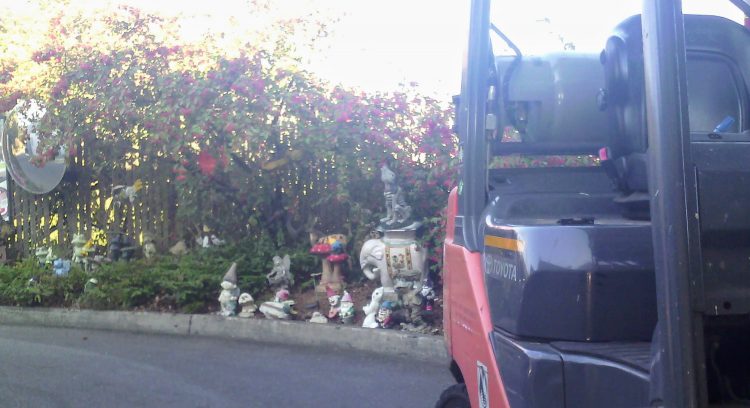 View past a forklift to a collection of garden gnomes and similar statues by a curb