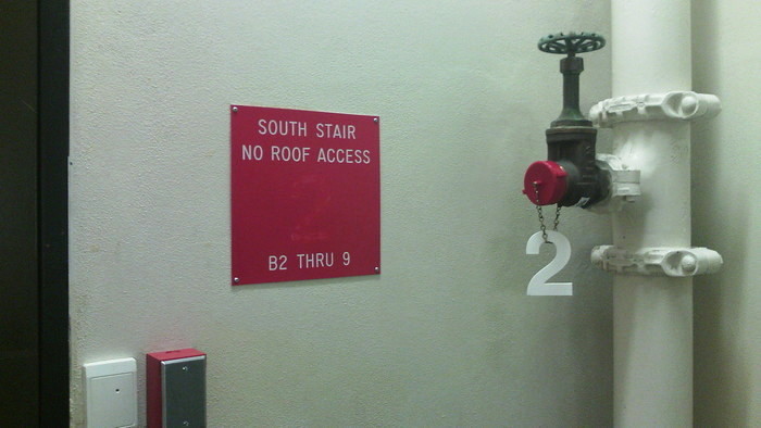 in a stairwell, the plastic 2 designating 2nd floor has fallen off its sign and been hung from a chain on a pipe valve
